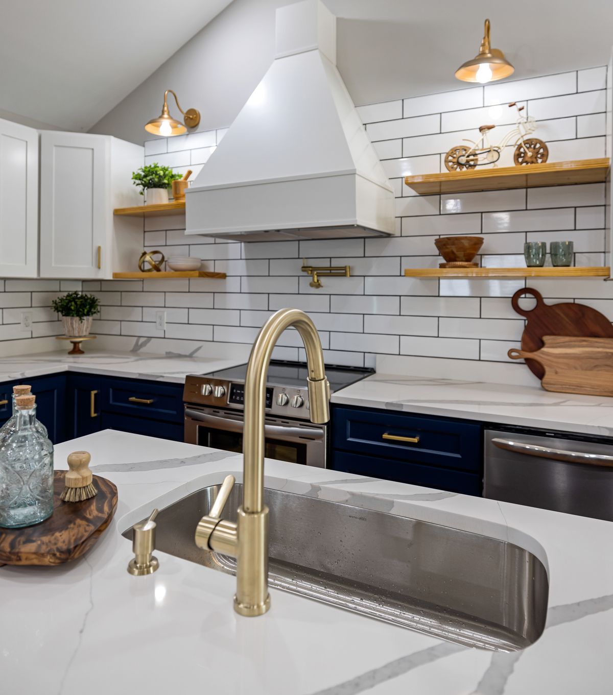 A brushed brass faucet and sconces paired with navy cabinets and stainless appliances