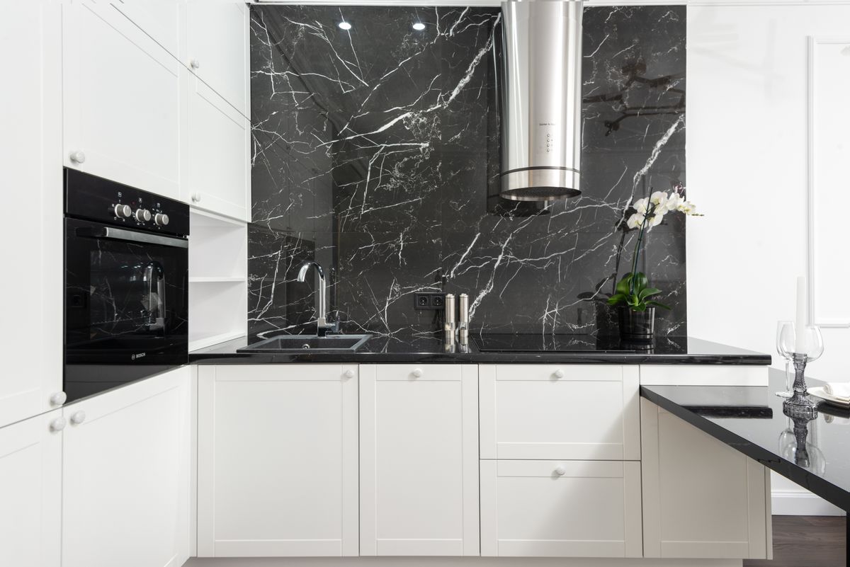 A dramatic full-height black marble slab backsplash with a statement range hood