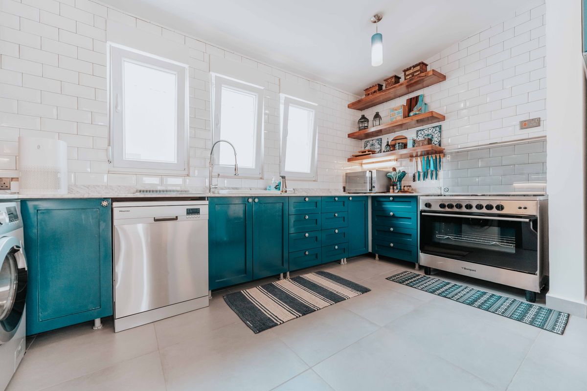 A two-tone kitchen with teal cabinets, white walls, and marble countertops